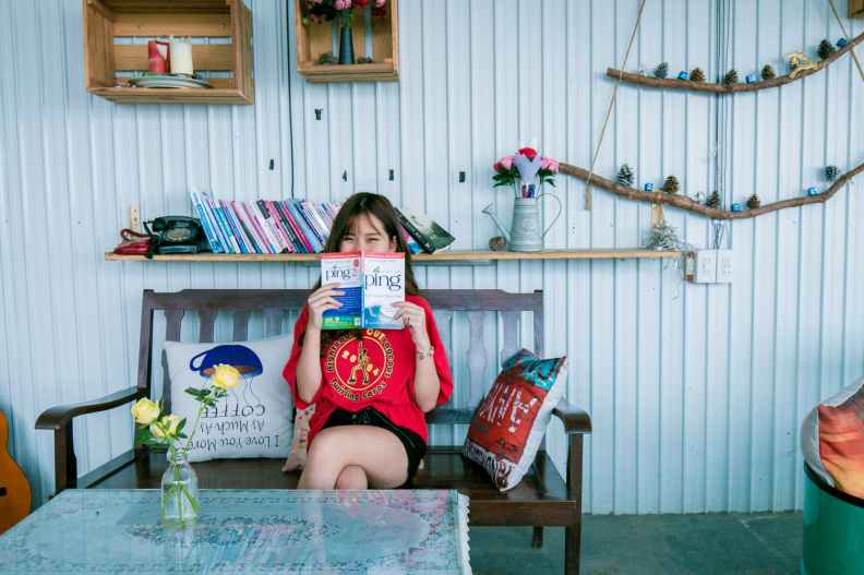 woman in red shirt holding book sitting on bench in front of coffee table